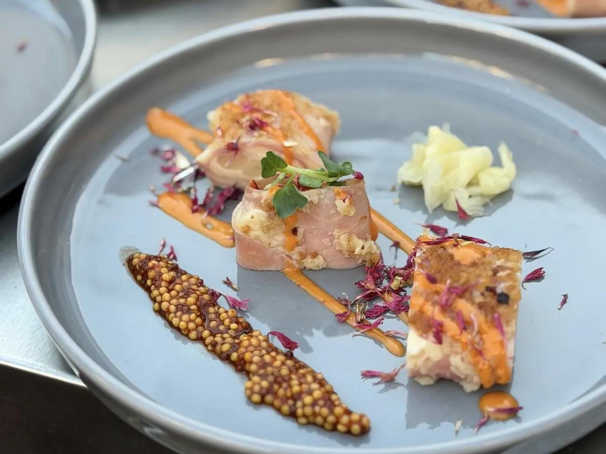 Fein angerichteter Teller mit Lachs-Röllchen, Senfkaviar, Orangensauce und essbaren Blüten