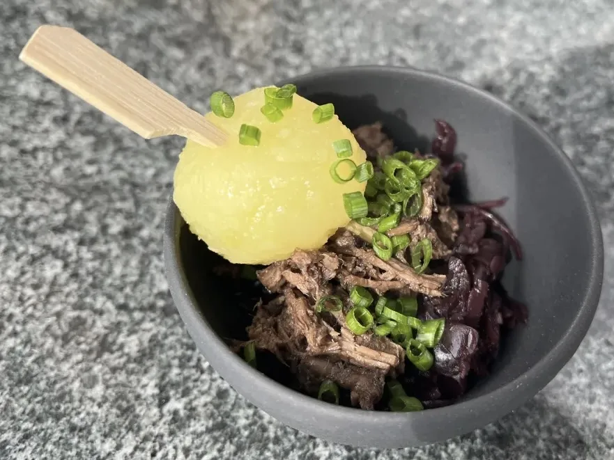 Schale mit zerzupftem Schmorfleisch, Rotkohl und Kartoffelkloß am Spieß, mit Frühlingszwiebeln garniert