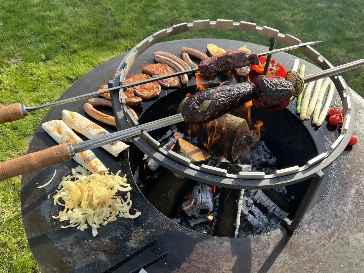 Feuerring mit Spießen, Bratwürsten, Steaks, Auberginen und weißem Spargel über der Glut