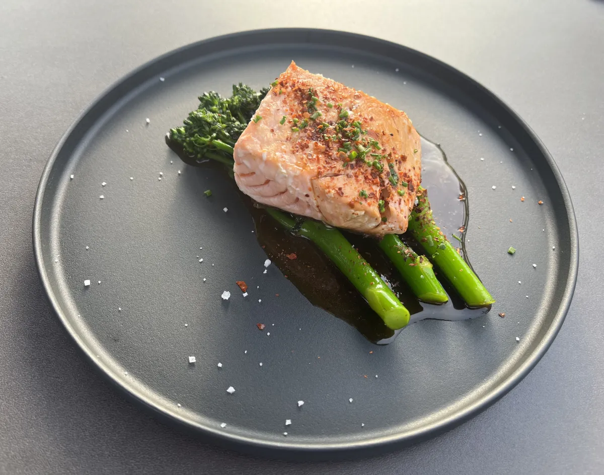 Gebratener Lachs auf grünem Brokkolini, serviert auf dunklem Teller